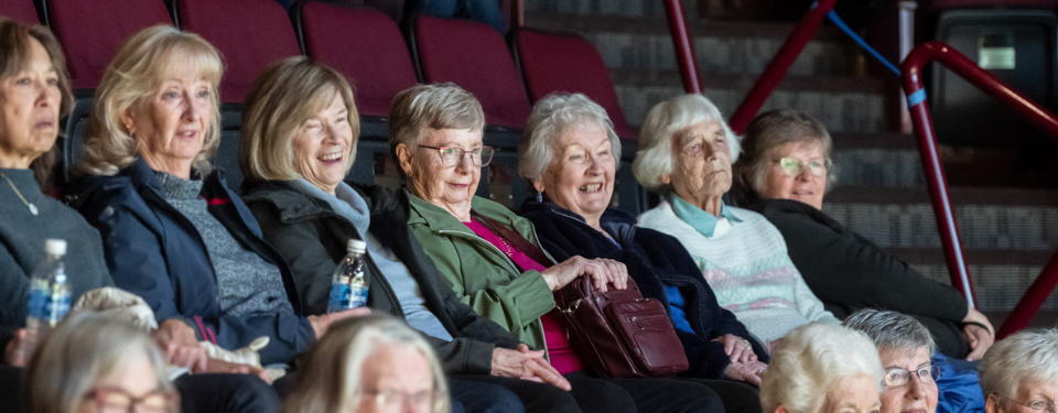 a row of women laughing in a theatre while they watch a play. the seats are red.